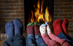 Photo of a family with colorful socks warming their feet in front of a blazing fire of cut, dried, split hardwood firewood from Fallowfield Tree Farm